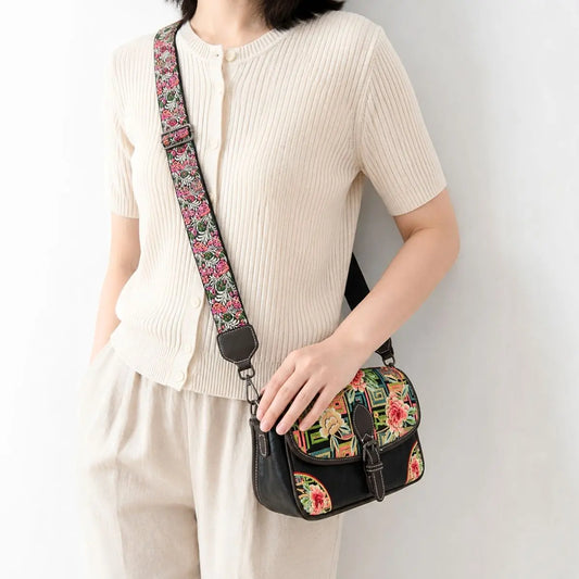 Black vintage saddle crossbody bag decorated with colorful peony geometric embroidery, paired with cream knit top, featuring adjustable floral wide shoulder strap for casual daily wear.