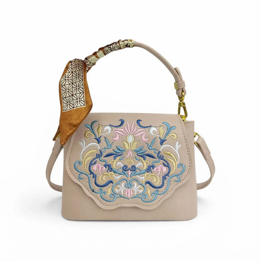 Beige leather crossbody handbag with traditional Chinese floral embroidery, printed silk scarf wrapped on top handle, golden hardware and detachable shoulder strap, product shot on plain white background