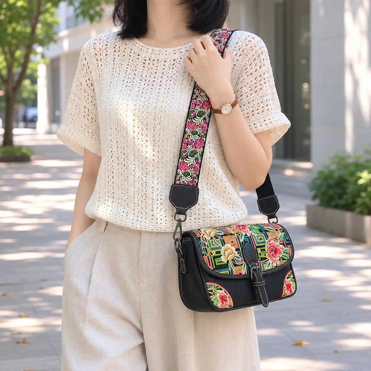 Black vintage saddle crossbody bag with colorful peony and traditional geometric embroidery, paired with hollow knit top for casual urban street daily styling.