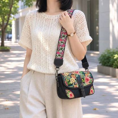 Black vintage saddle crossbody bag with colorful peony and traditional geometric embroidery, paired with hollow knit top for casual urban street daily styling.