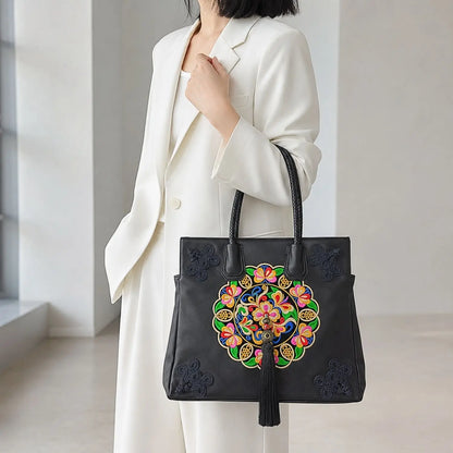 Black ethnic floral leather tote hand carried with white formal suit in minimalist bright office space, perfect for elegant daily business commuter wear. 