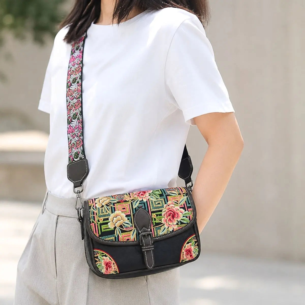 New Chinese style black floral embroidered saddle crossbody bag with adjustable wide floral shoulder strap, matched with simple white short sleeve tee for commuter outfits.