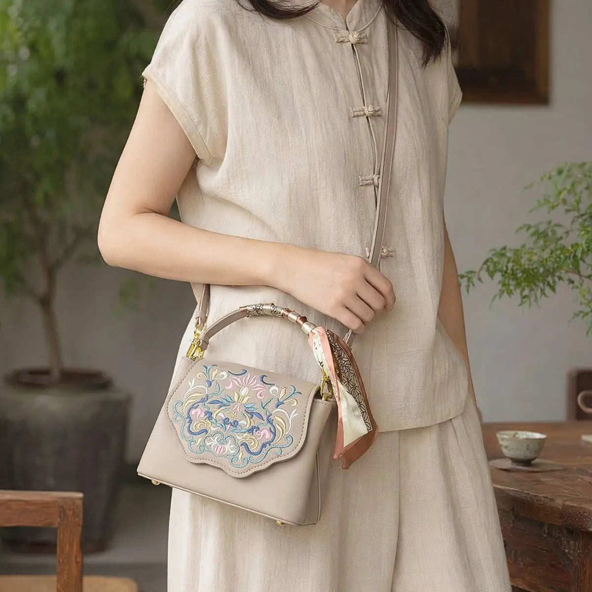 Woman in beige traditional linen outfit crossbody embroidered leather handbag with silk scarf, indoor oriental tea room quiet scene
