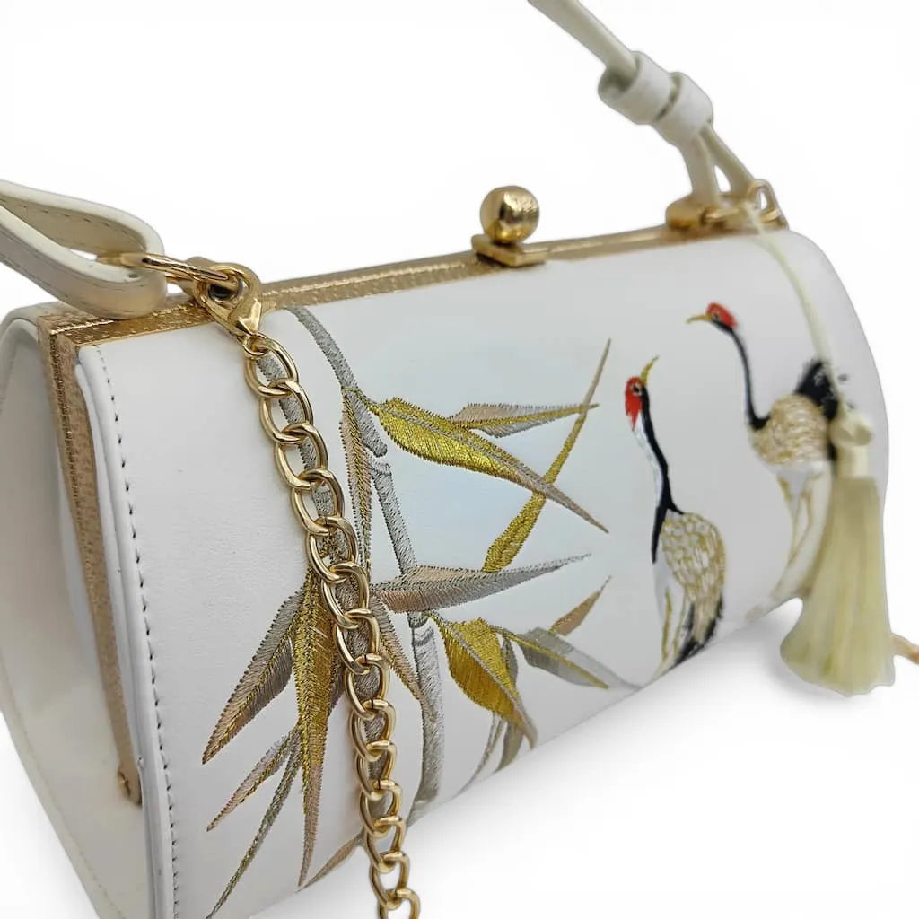 close‑up side shot of golden bamboo and red‑crowned crane embroidery on white clutch bag