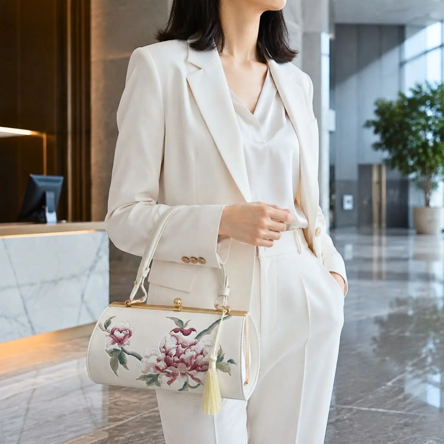 White peony embroidered barrel clutch paired with white formal suit, modeled in modern lobby, ideal for elegant business and commuter styling.