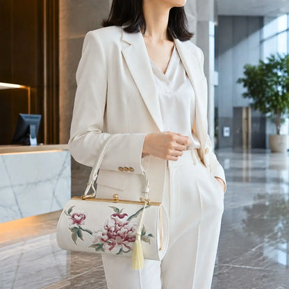 White peony embroidered barrel clutch paired with white formal suit, modeled in modern lobby, ideal for elegant business and commuter styling.