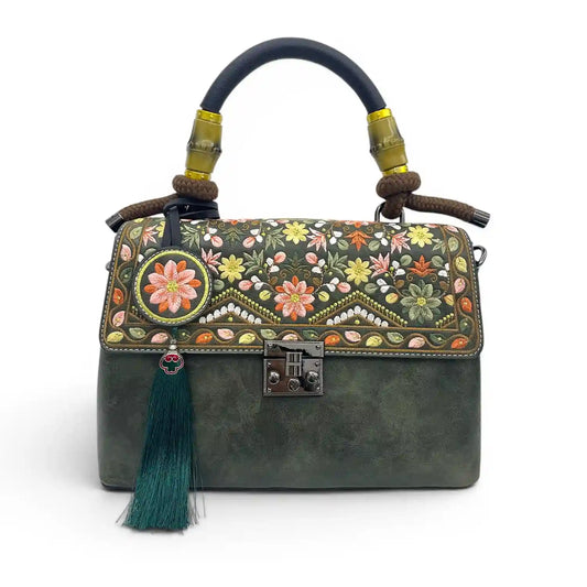 Dark green vintage leather handbag with delicate floral embroidery, bamboo top handle, green Chinese tassel and retro metal lock, studio product shot on pure white background