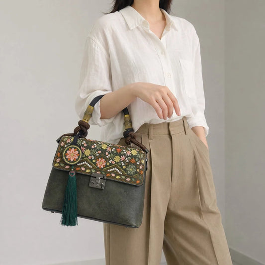 Faceless Asian woman carries dark green vintage handbag under arm, wearing white linen shirt and khaki trousers, plain light gray indoor workplace background