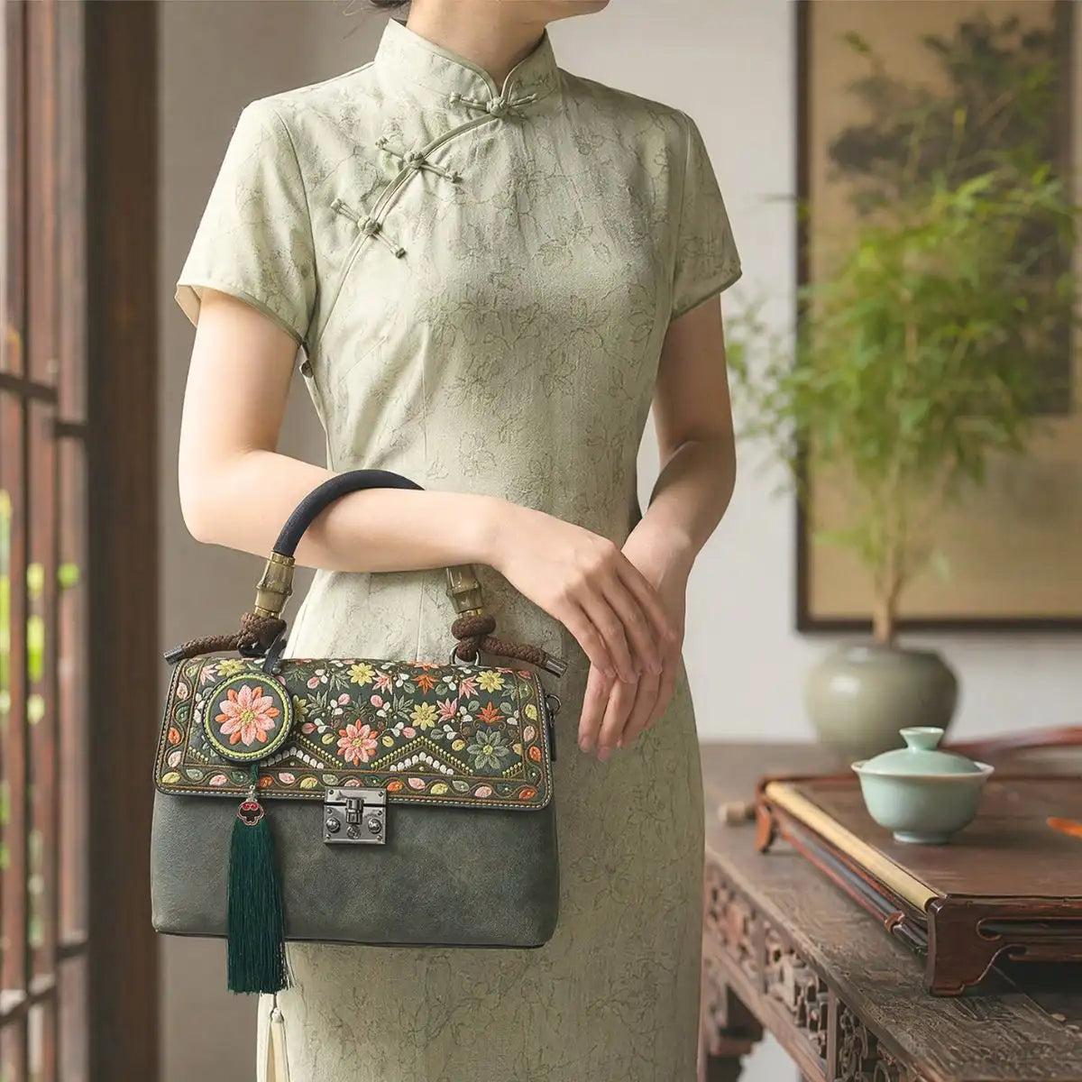 Faceless woman in light green jacquard cheongsam holds dark green embroidered handbag, traditional Chinese tea room interior with wooden table, plants and tea set