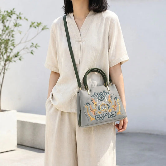 Gray oriental embroidered leather tote worn crossbody with detachable dark green strap, matched with beige linen casual outfit for daily street styling.