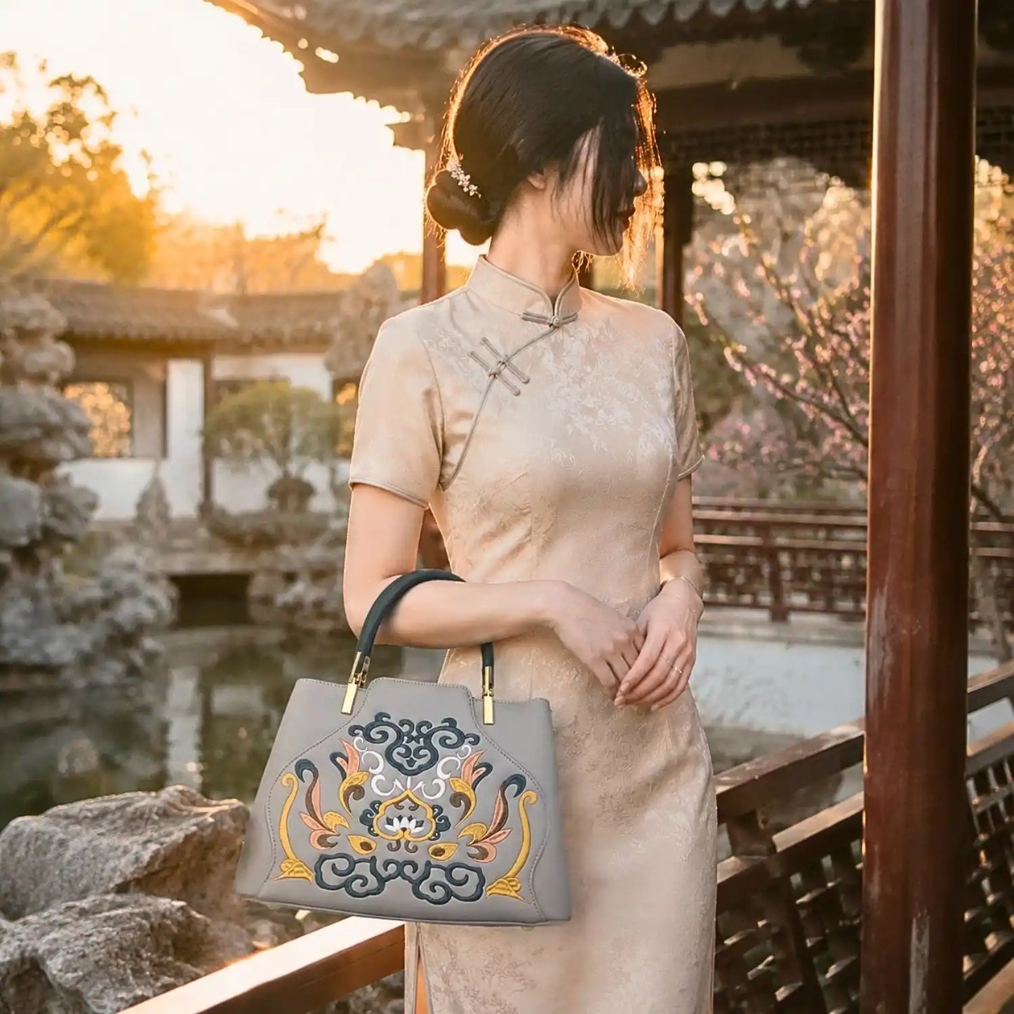Gray embroidered leather handbag paired with beige cheongsam, modeled in a traditional Chinese garden pavilion at warm sunset for oriental outfit inspiration.