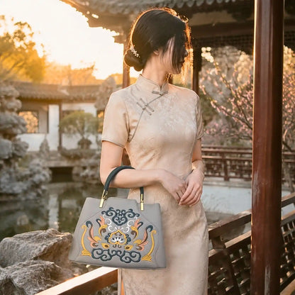 Gray embroidered leather handbag paired with beige cheongsam, modeled in a traditional Chinese garden pavilion at warm sunset for oriental outfit inspiration.