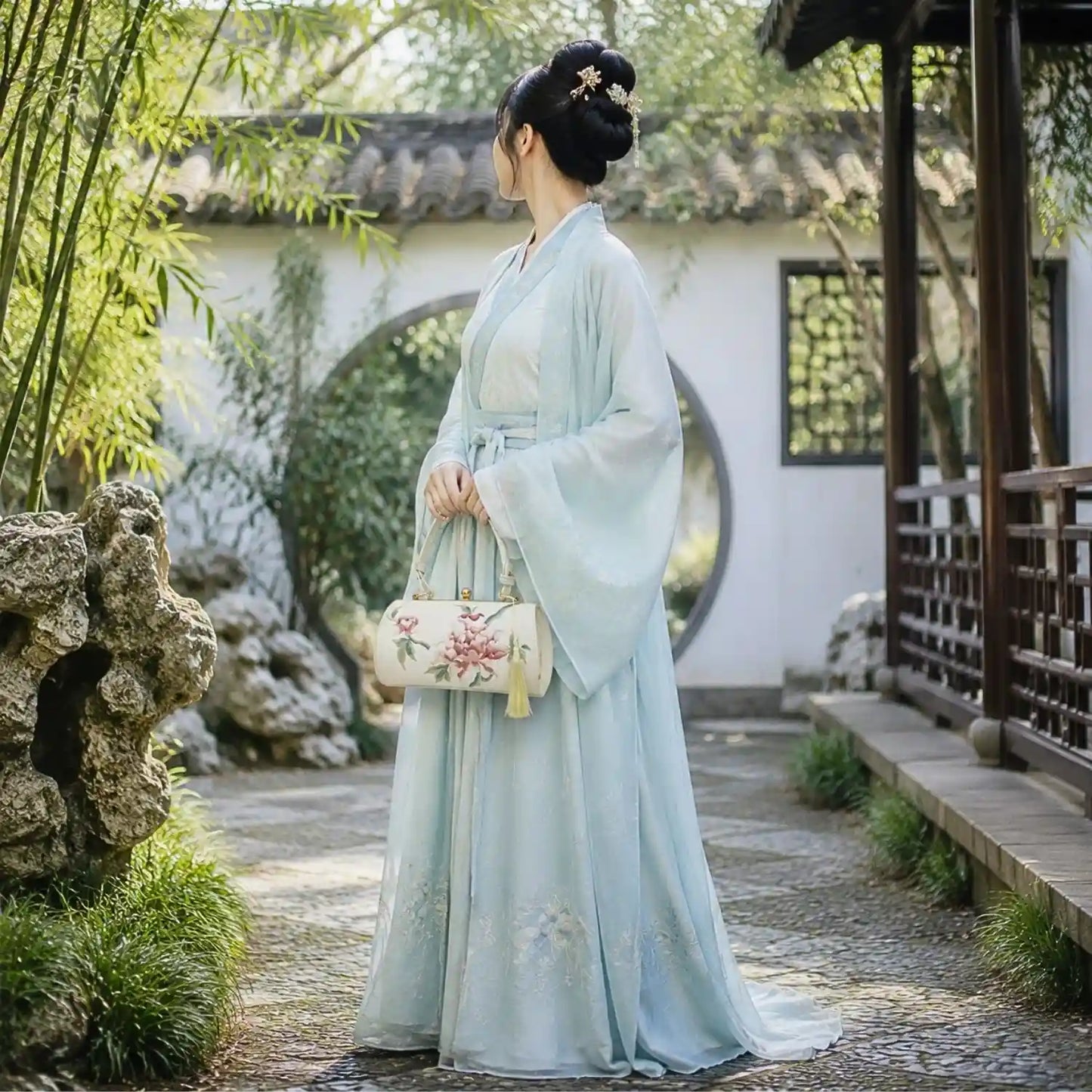 White peony embroidered top handle handbag matched with light blue hanfu, photographed in traditional Chinese ancient garden scenic courtyard.