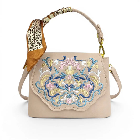 Beige leather crossbody handbag with traditional Chinese floral embroidery, printed silk scarf wrapped on top handle, golden hardware and detachable shoulder strap, product shot on plain white background