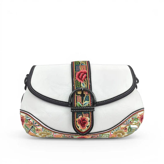 Soft white PU leather saddle crossbody bag adorned with colorful vintage peony floral embroidery and ethnic geometric trim, fitted with a metal buckle strap, displayed on a minimalist white background.