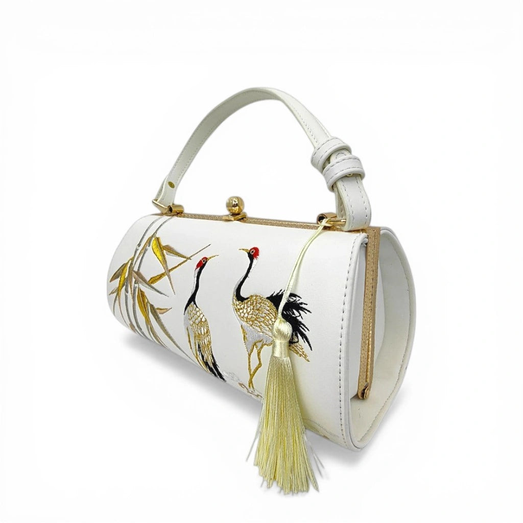 three‑quarter view of white pu leather clutch bag with double crane and bamboo embroidery, cream tassel decoration