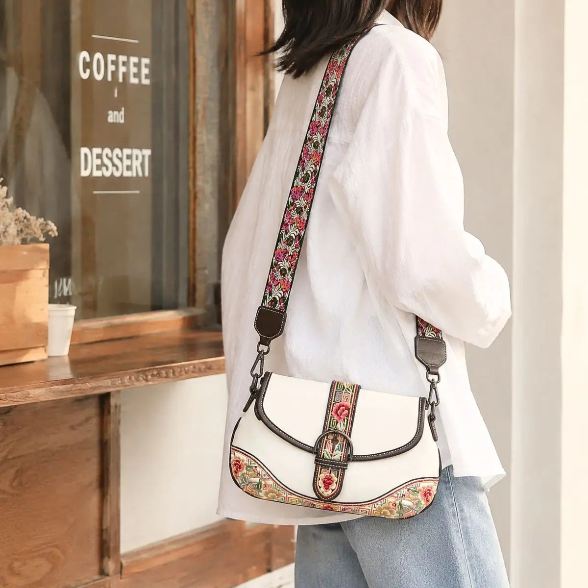 White floral embroidered saddle crossbody bag paired with white shirt and jeans, modeled outside retro coffee shop for casual street fashion look.