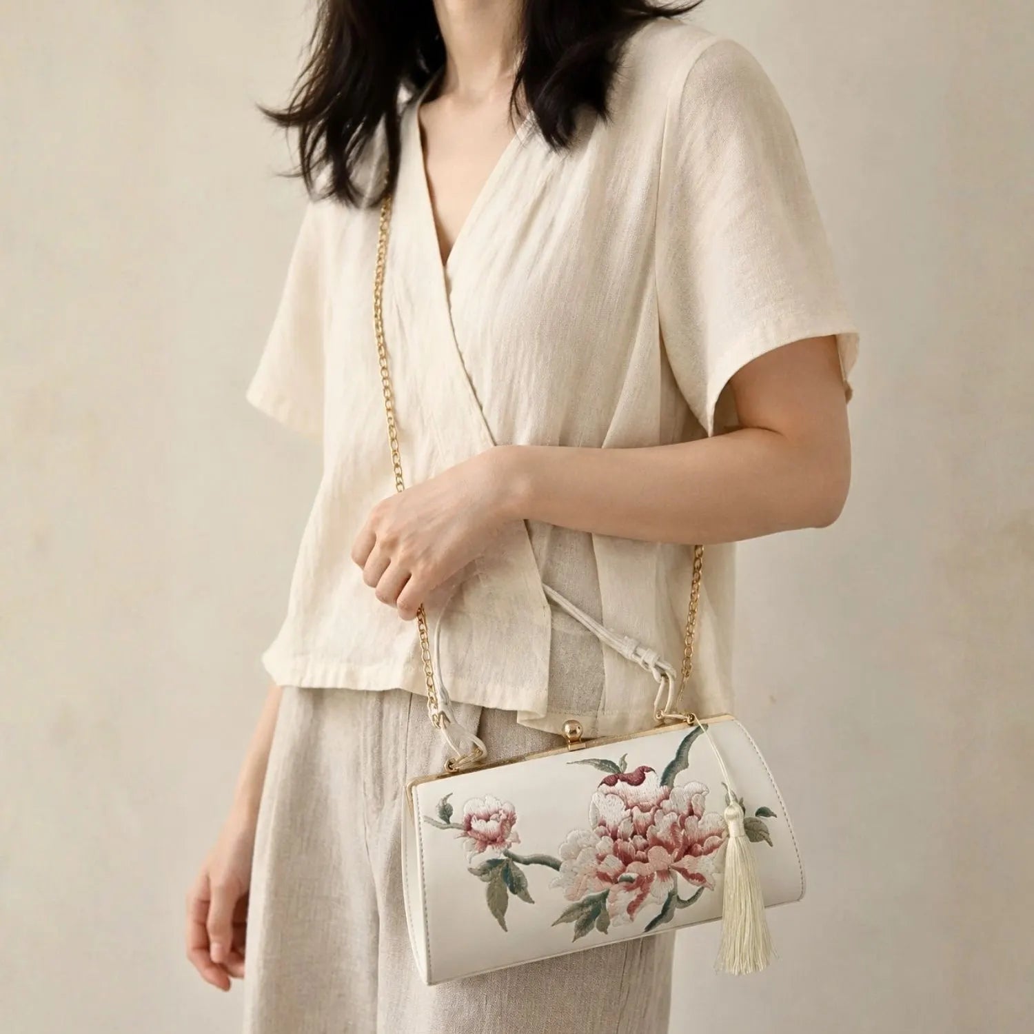 White peony embroidered barrel bag worn as chain crossbody with casual beige linen top, minimalist indoor daily lifestyle fashion shot.